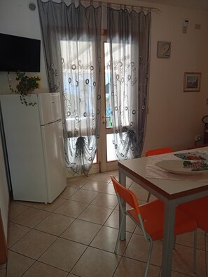 A kitchen with a refrigerator, a dining table with chairs, and a window with curtains.