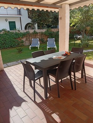 An outdoor patio with a table and chairs, a covered area, and a view of a garden and building.