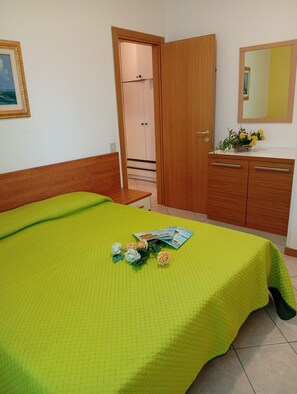 A bedroom with a bed, a wooden wardrobe, a bedside table, a mirror, and a framed picture on the wall.