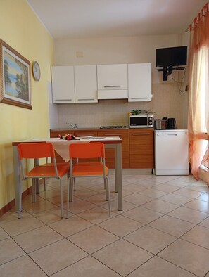 A small kitchen with white cabinets, a microwave, a toaster, and a refrigerator. There is a dining table with two chairs.