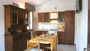 Een kleine keuken met houten kastjes, een eettafel met stoelen en een inbouwfornuis.