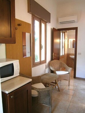 Una cocina funcional con microondas, muebles de mimbre y vistas a través de una puerta.