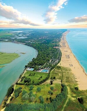 An aerial view of a coastal area with a beach, a swimming pool, and surrounding greenery.