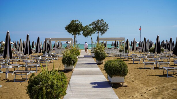 A beachside walkway with rows of sun loungers and potted plants. - Residenz Elia Wohnung Bilo Erdgeschoss für 5 Personen (Bibione)