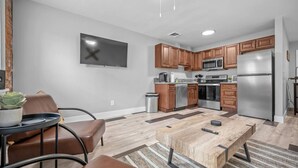 A modern kitchen with wooden cabinets, stainless steel appliances, and a flat-screen TV mounted on the wall. - Rhythm Loft Above the Honky Tonk (Saint Charles)