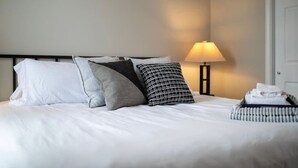 A neatly made bed with pillows, a bedside lamp, and a stack of towels. - Rhythm Loft Above the Honky Tonk (Saint Charles)