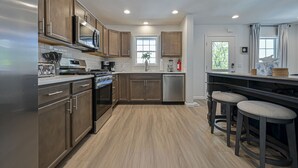 A modern kitchen with wooden cabinets, stainless steel appliances, and a bar area with stools.