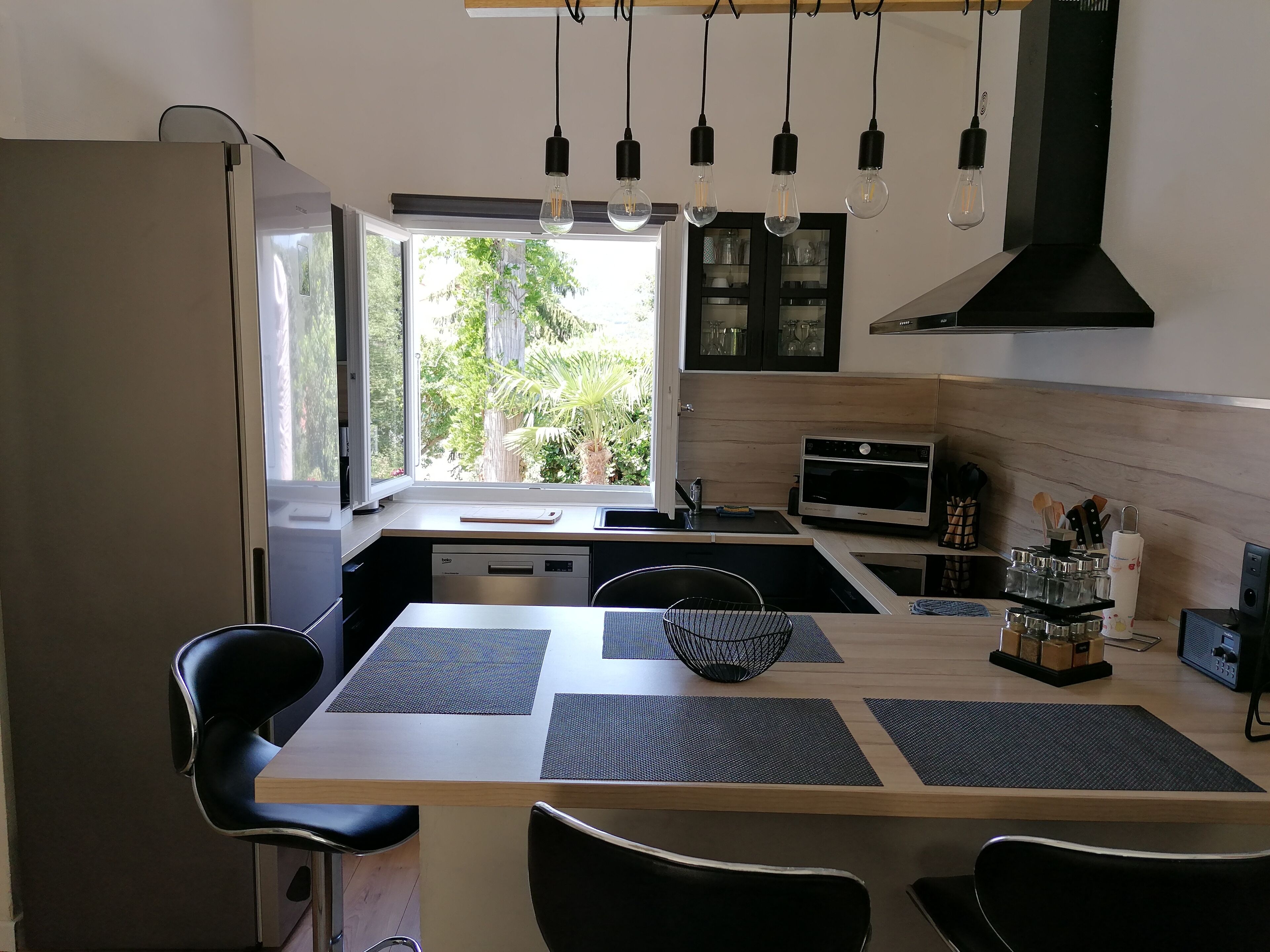 Eine moderne Küche mit Essbereich, ausgestattet mit Backofen, Mikrowelle und einem großen Fenster mit Blick auf Grünflächen.