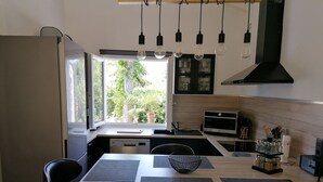 A modern kitchen with a dining area, featuring a built-in oven, a microwave, and a large window with a view of greenery outside. - Charming Quiet House in Reynes Close to Les Cures and the Côte Vermeille (Reynes)