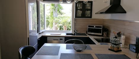 Una cocina moderna con comedor, que cuenta con un horno empotrado, un microondas y un amplio ventanal con vistas al exterior.