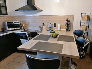 Una cocina moderna con microondas integrado, cocina a gas y campana extractora de acero inoxidable. Hay una mesa de comedor con cuatro sillas y un frutero encima.
