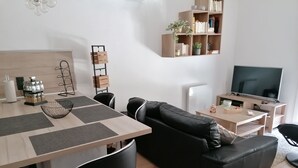 A modern living room with a wooden dining table, black leather sofa, and a TV on a wooden stand. - Charming Quiet House in Reynes Close to Les Cures and the Côte Vermeille (Reynes)
