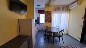 Eine kompakte Küche mit Kühlschrank, Mikrowelle und Waschmaschine, ein Essbereich mit Tisch und Stühlen sowie ein großes Fenster mit Vorhängen.