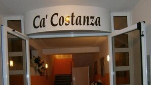 Ein Hotel Eingang mit einem Schild, auf dem 'Ca' Costanza' steht, einer Treppe und einem Empfangstresen.