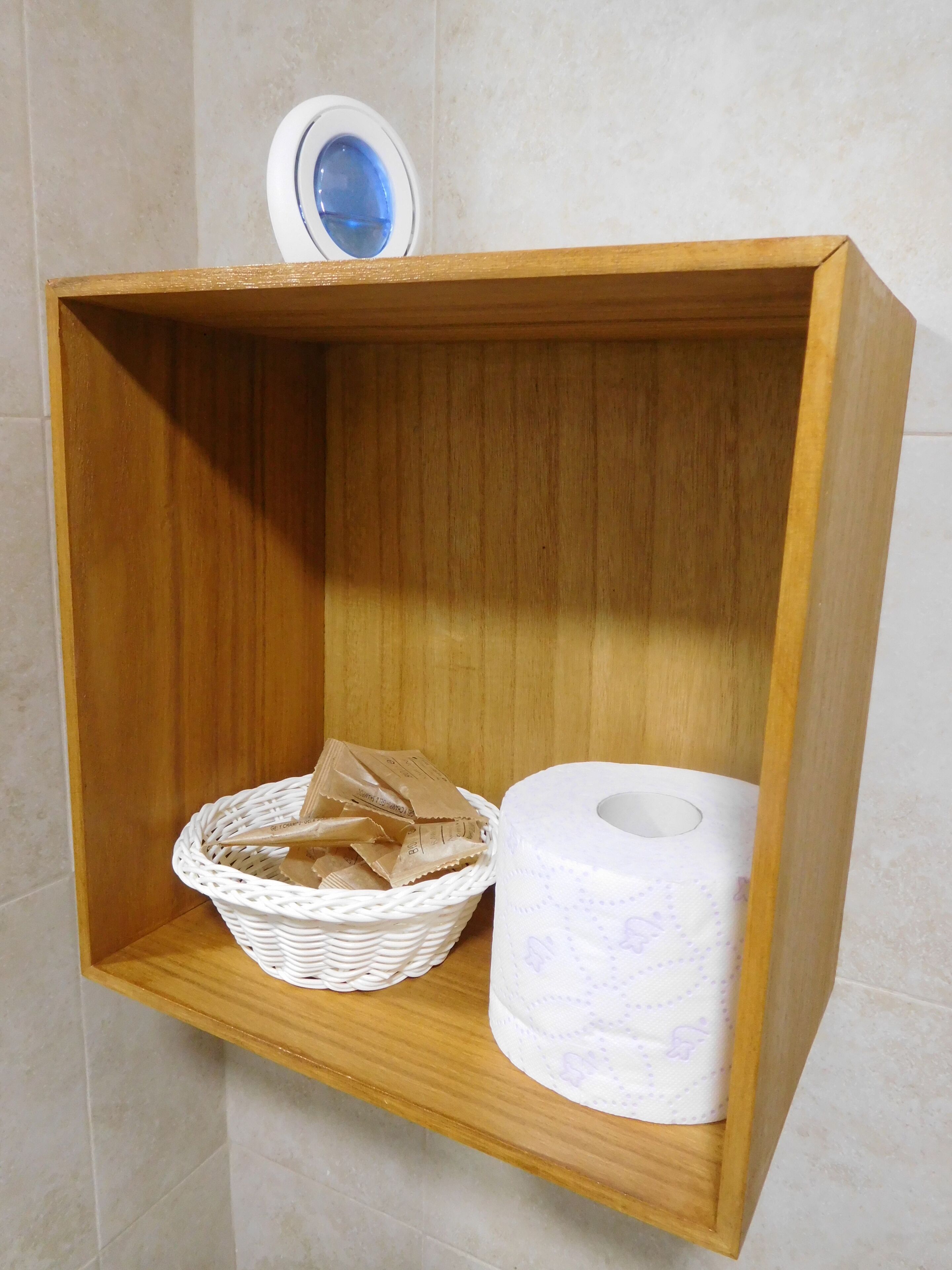 A wooden shelf with a white wicker basket containing brown paper bags and a roll of toilet paper.