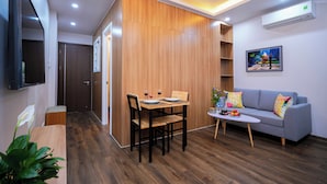 A modern living room with a wooden partition, a grey sofa, a small table with fruit, and a TV mounted on the wall. - Fusion Gates Apartment (Hanoi)