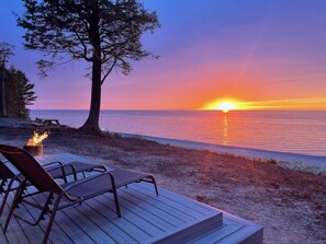 Auringonlaskunäkymä terassilta, jossa on tuoleja ja nuotiopaikka.