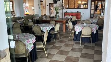 A dining area with checkered flooring, round tables with floral tablecloths, and chairs with cushioned backs.