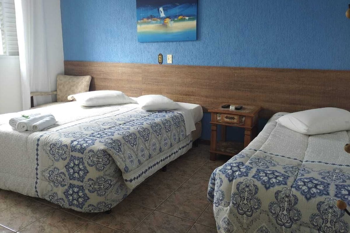 Hotellihuone, jossa on kaksi sänkyä, seinällä taulu ja pieni puinen pöytä.