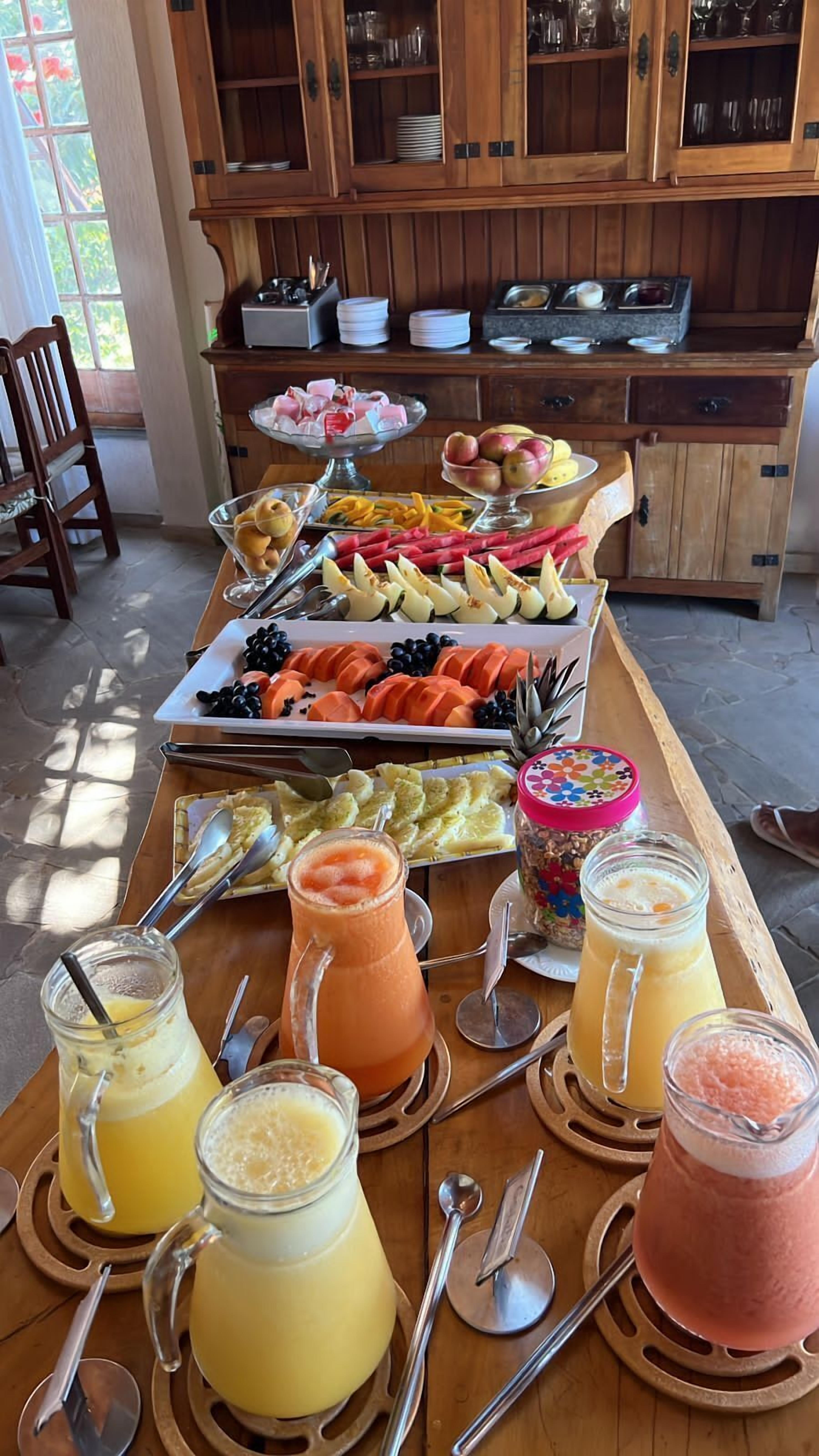 Um buffet de café da manhã com diversas frutas, legumes e bebidas sobre uma mesa de madeira.