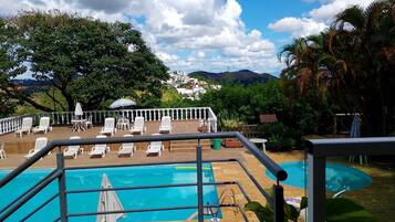 Une piscine entourée de chaises longues et de parasols, bordée de verdure et offrant une vue sur une ville au loin.