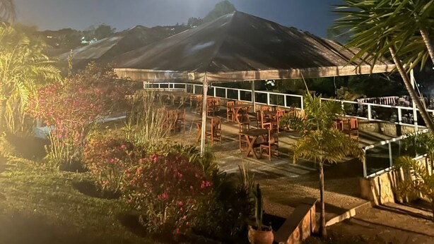 Vista nocturna de un resort con zona de comedor, asientos al aire libre y montañas al fondo.