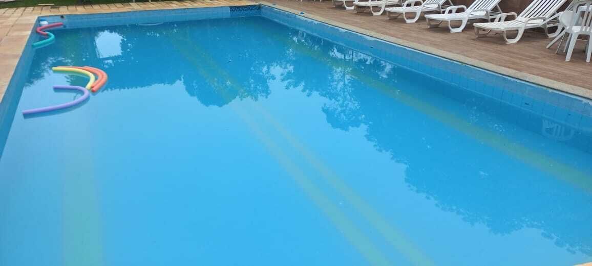Una piscina con agua azul cristalina, rodeada de sillas reclinables blancas.