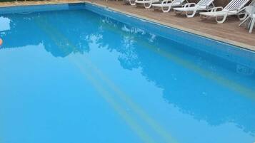 Una piscina con agua azul cristalina, rodeada de sillas reclinables blancas.