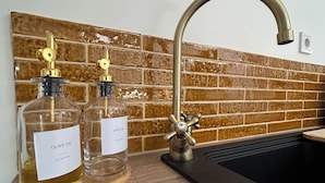 Ein Küchenspülbecken mit einem modernen Wasserhahn, zwei Glasflaschen Olivenöl und einer Holztablett.