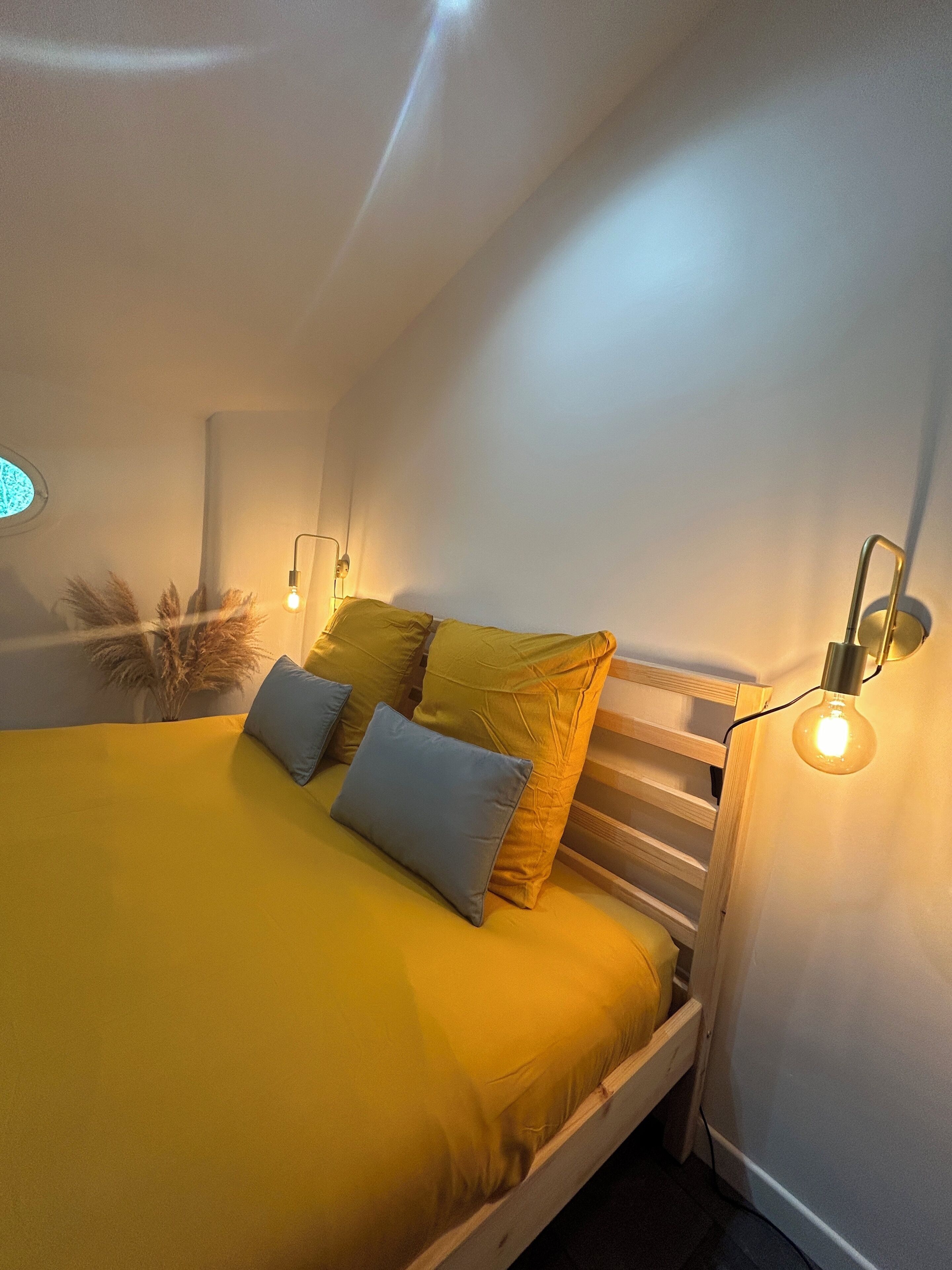 A bed with yellow bedding, two pillows, and a wooden headboard. There are two wall-mounted light fixtures on either side of the bed.