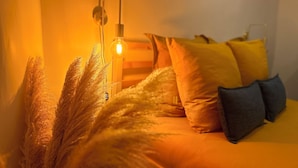 Ein Bett mit gelben und grauen Kissen, einer Wandlampe und einer Zimmerpflanze.