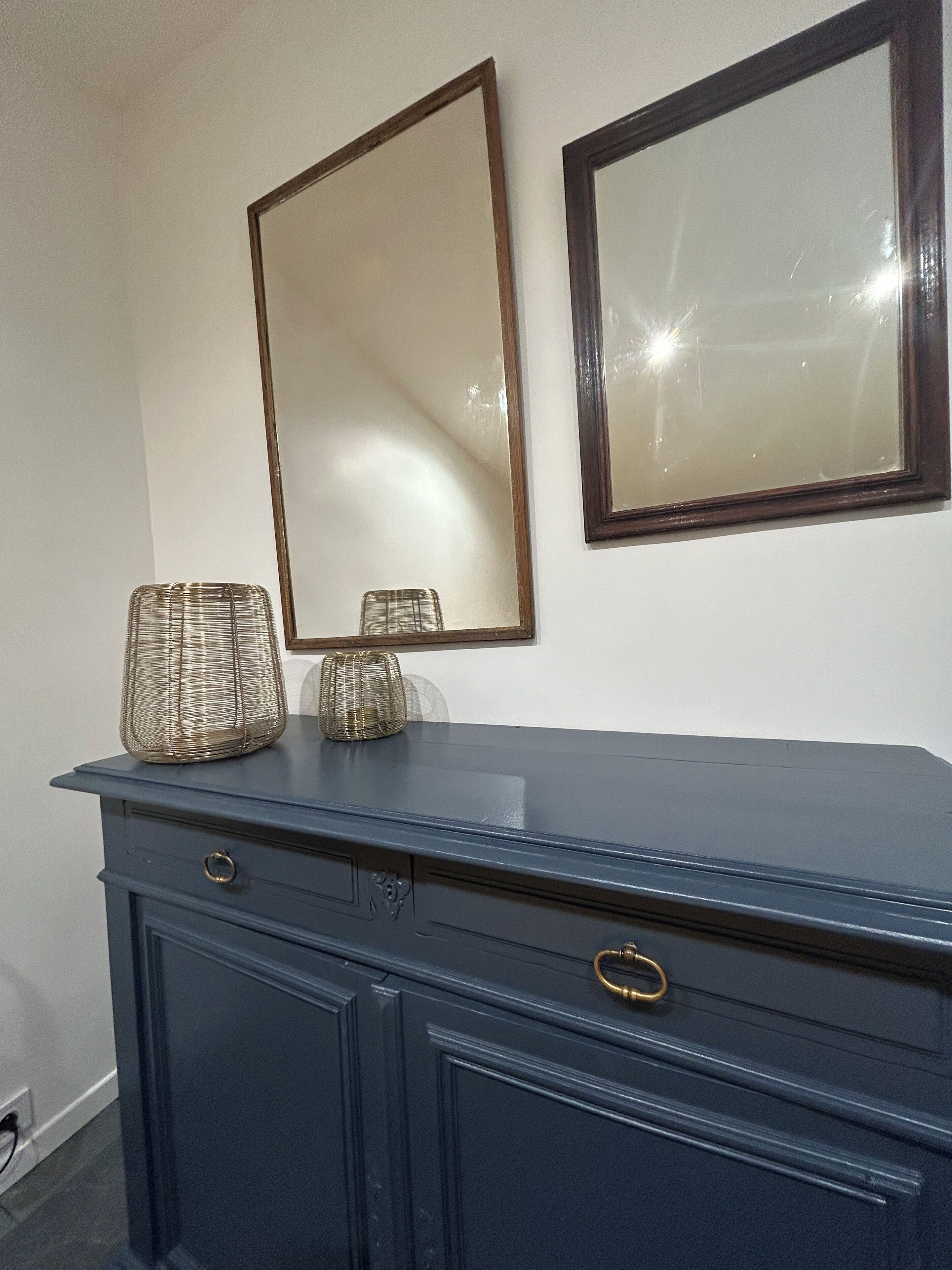 A dark blue dresser with two drawers and a small round mirror above it.