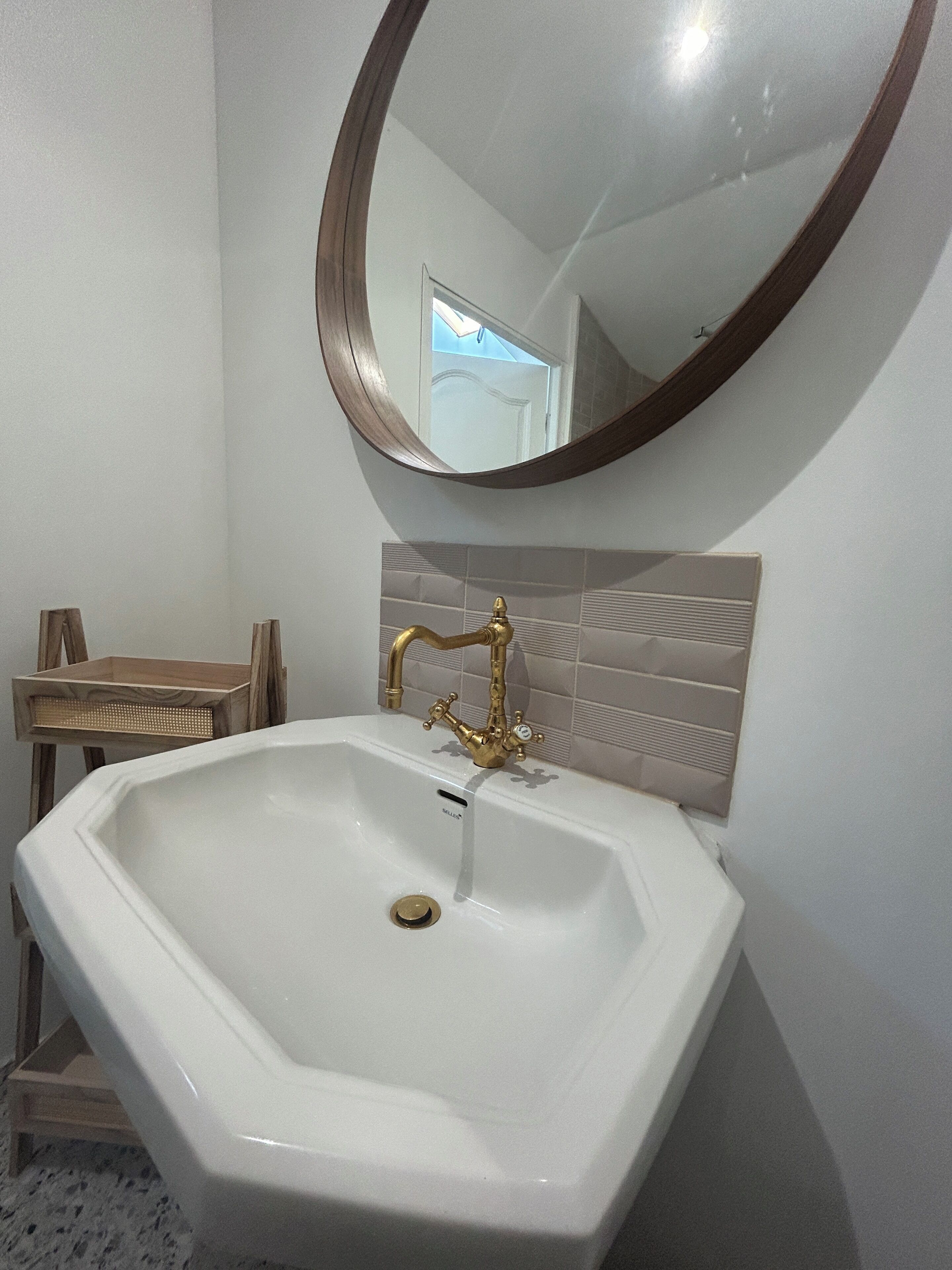Un baño con un lavamanos blanco, grifos dorados y un taburete de madera.