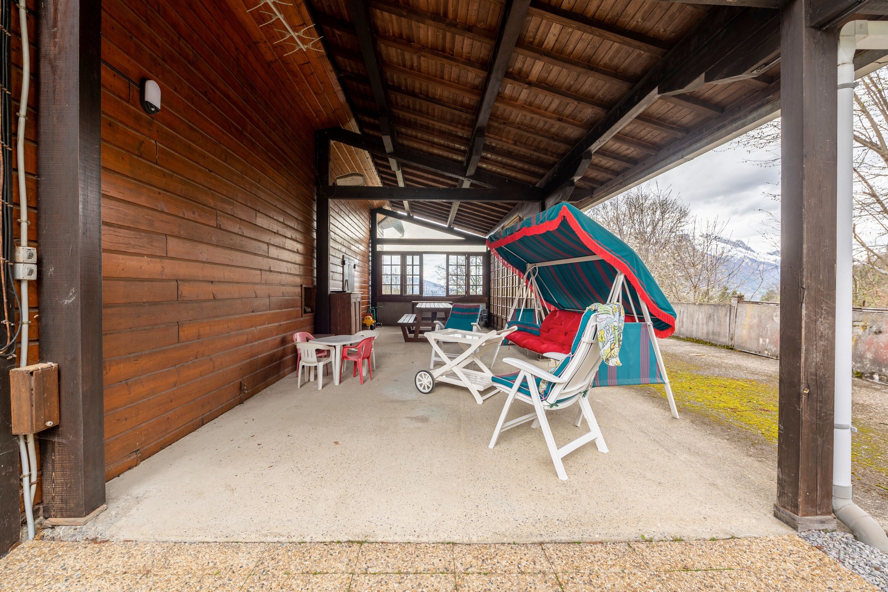 A covered outdoor seating area with wooden walls, a concrete floor, and a view of mountains in the background.