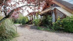 Une maison traditionnelle en bois, avec un toit de chaume, entourée de chemins de gravier et de différentes plantes.