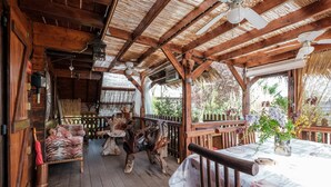 Une terrasse en bois surmontée d’un toit de chaume, avec des meubles en bois et une table recouverte d’une nappe blanche.