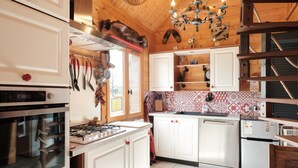 Une cuisine avec des meubles blancs, une cuisinière à gaz, un four en acier inoxydable et un porte-casseroles suspendu.