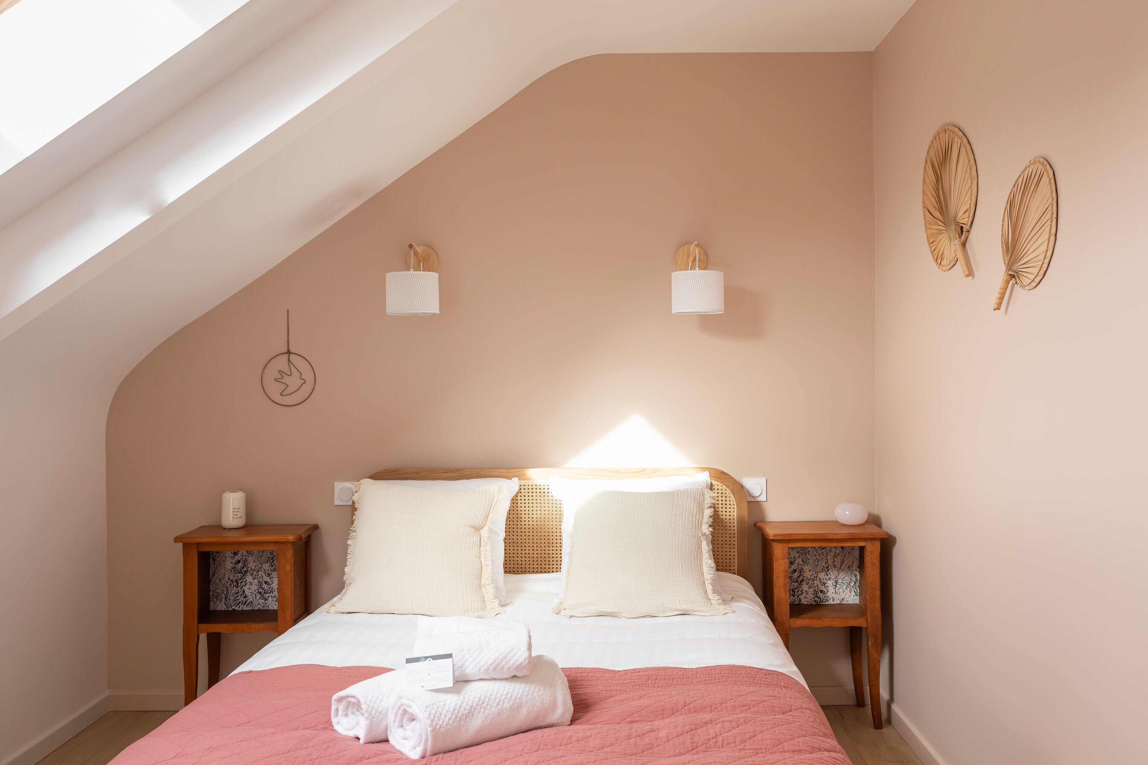 Ein Schlafzimmer mit schrägen Wänden, einem Bett mit weißer Bettwäsche, zwei Nachttischen mit Lampen und Wanddekoration.