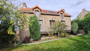 Une maison en pierre dotée d’un balcon, entourée de jardins et d’arbres bien entretenus.