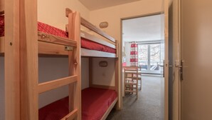 Habitación con literas, un escritorio y silla de madera, una puerta que da a un balcón y una ventana con cortinas.