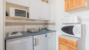 Una cocina compacta equipada con microondas, un refrigerador pequeño, lavavajillas y armarios de madera.