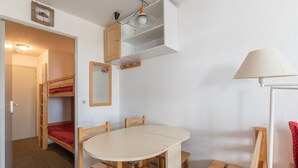 Habitación pequeña con literas, una mesa redonda con sillas, una lámpara y un estante con un espejo.