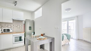 A modern kitchen with white cabinets, a microwave, and an oven. There is a dining table with placemats and a candle. The room has a large window and a view of buildings outside.