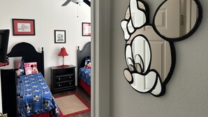 A child's bedroom with a Mickey Mouse mirror, a ceiling fan, and a bed with a Mickey Mouse themed bedspread.