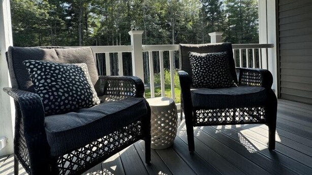 A covered porch with two wicker chairs and a white railing.