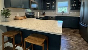 A modern kitchen with dark cabinets, a large island with stools, stainless steel appliances, and pendant lighting.
