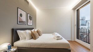 Une chambre moderne avec un grand lit, une table de chevet avec une lampe et une vue sur un balcon.