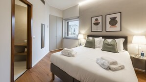 Une chambre d’hôtel avec un grand lit, une table de chevet avec une lampe, une fenêtre donnant sur un beau paysage et des œuvres d’art accrochées au mur.