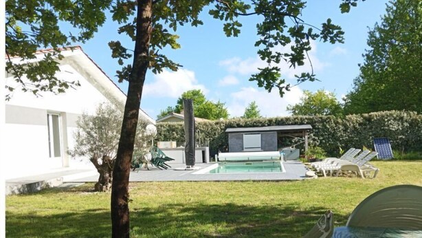 Un área de piscina moderna al aire libre con una silla de descanso, un edificio pequeño y un árbol.