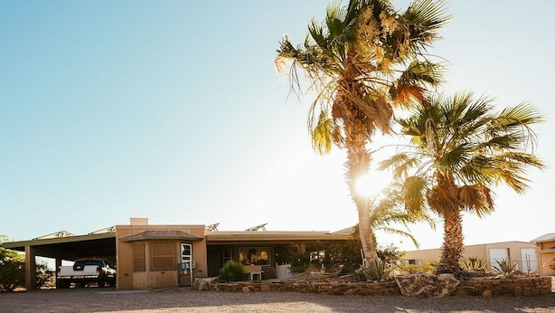 A modern house with a garage, a covered patio, and a palm tree in the foreground. - Secluded and Secure, Pet-friendly Desert Getaway. Your vacation awaits! (Lake Havasu City)